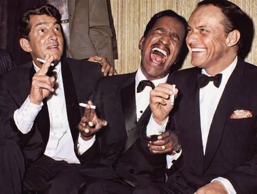 Frank Sinatra, Dean Martin, and Sammy Davis Jr. laughing together on stage at the Sands Hotel in 1960.